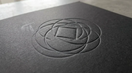 Gros plan sur un logo en relief gaufré sur la couverture d'une plaquette commerciale, montrant les détails de texture et les jeux de lumière sur la surface